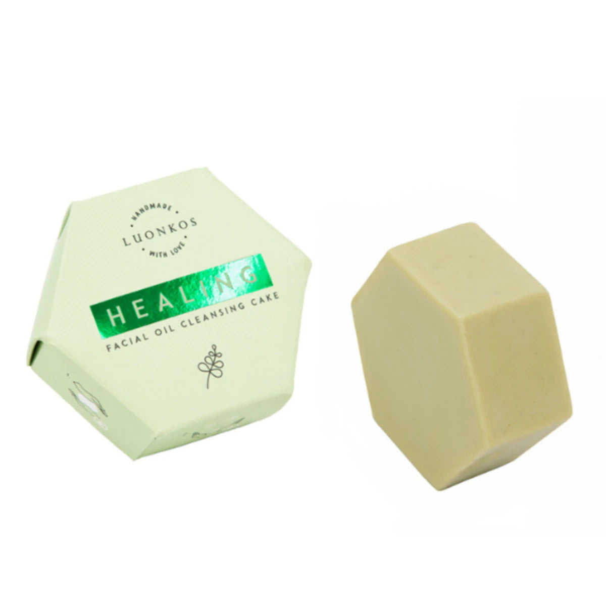 Luonkos Healing Facial Oil Cleansing Cake -kuusikulmainen kasvopuhdistuspala ja vastaava kuusikulmainen pakkaus valkoisella taustalla, tarjoaa ravitsevan öljypohjaisen puhdistuksen; pala kiinteä ja mattapintainen vaalean neutraalin sävyinen; pakkaus pahvia lihavoidulla mustalla tekstausvapaalla kirjasimella ja kultaisin korostuksin etupaneelissa; ei ihmisiä tai käsiä näkyvissä; kuva otettu ylhäältäpäin.