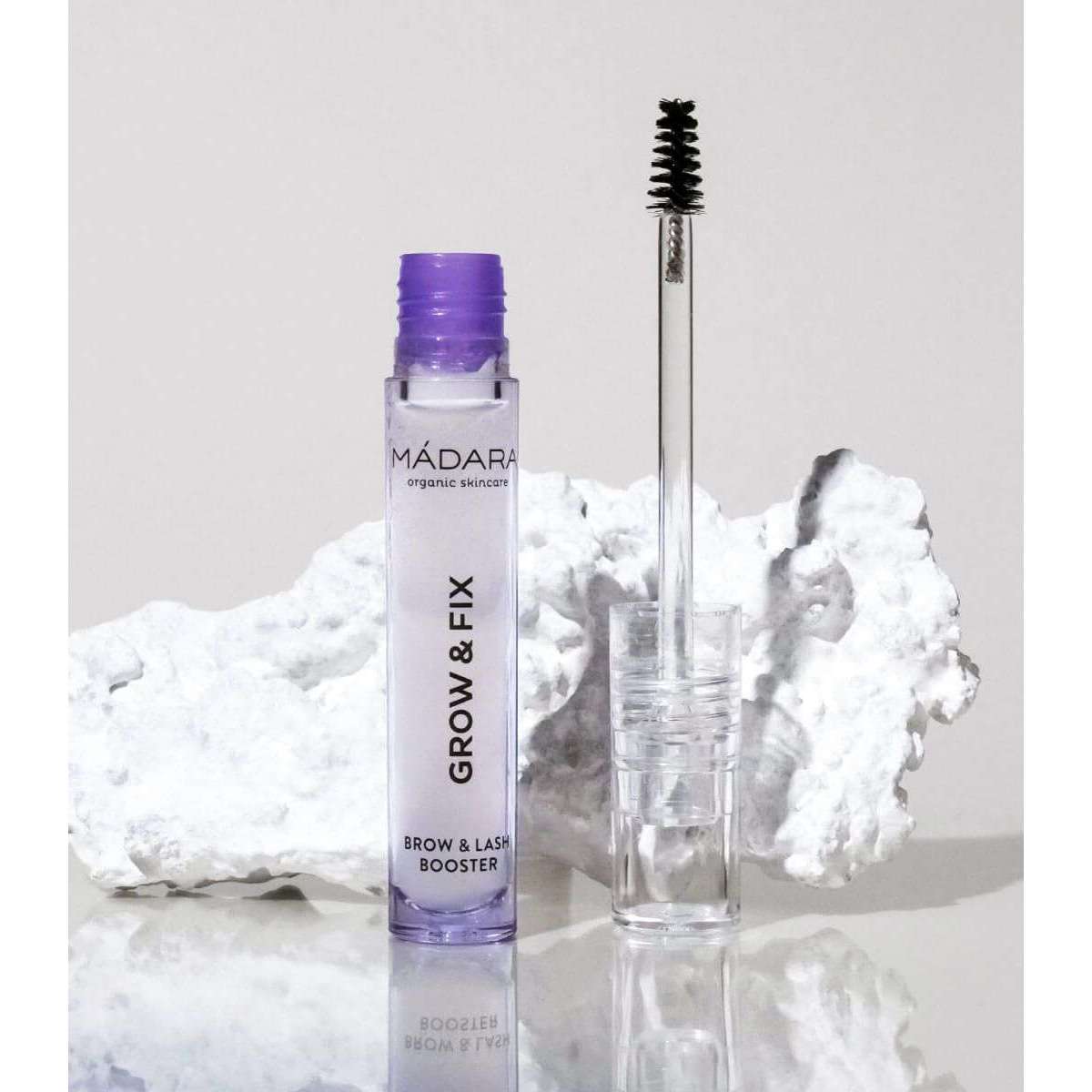 Madara Grow & Fix Kulmaseerumi; MÁDARA Grow & Fix Brow & Lash Booster -tuubi kirkkaan sauva-applikaattorin vieressä; tuubi valkoinen kiiltäväpinnalla ja lieriömäinen muoto, brändinimi ja tuoteotsikko mustin groteskikirjaimin; applikaattorin kahva kirkas ja harjakset näkyvissä; taustalla valkoisia tekstuurisia kiviä; ei ihmisiä tai käsiä, tuote pystyssä tasaisella pinnalla.