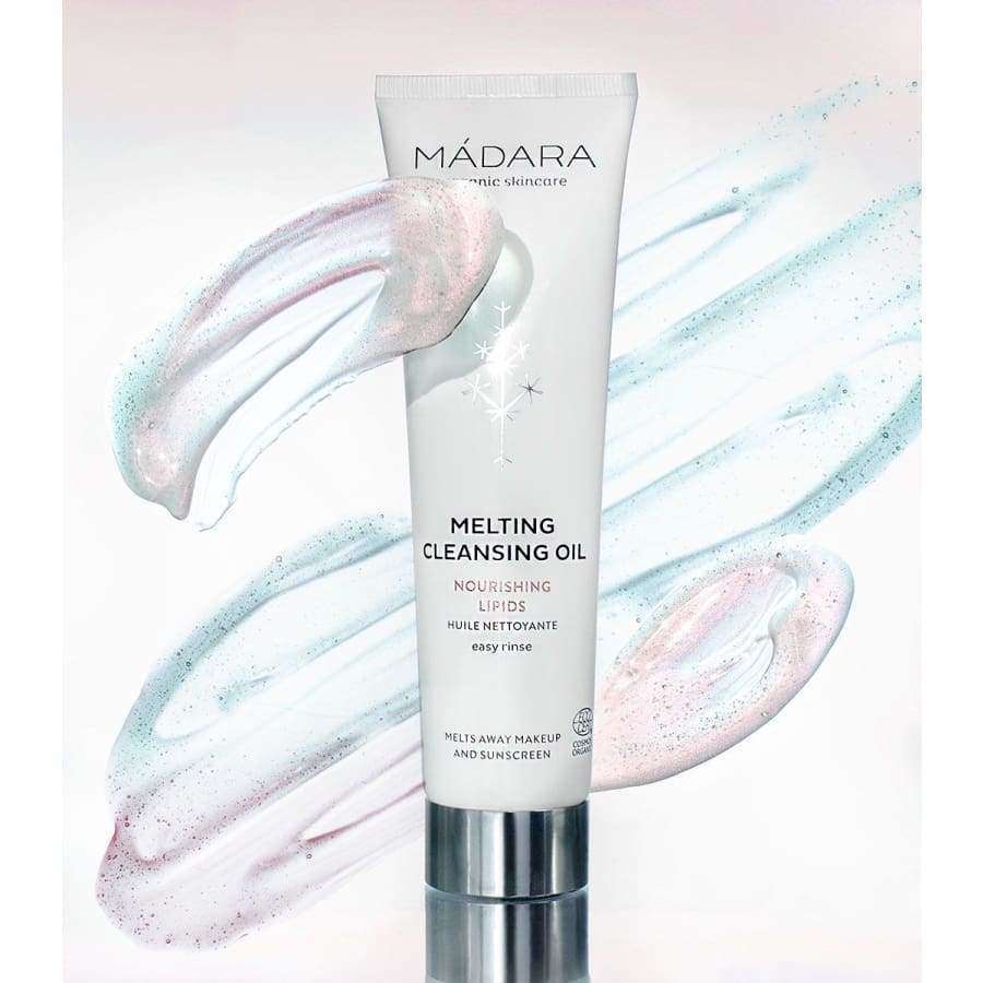Mádara Melting Cleansing Oil -puhdistusöljy; putkilo pystyssä, puolikiiltävää materiaalia vaalean, neutraalin sävyisenä; groteskiteksti painettuna etuosaan kontrastisin sävyin, kertaalleen näkyvissä tuotenimi ja käyttötiedot; tausta minimalistinen ja vaalea, näkyvissä pastellisävyisiä kiehkuroita ja kimalluksia; ei ihmisiä tai käsiä kuvassa.