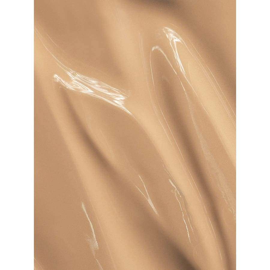 MÁDARA Skin Equal Meikkivoide, sävy Sand; sileä, ruskehtava pinta kiiltävin heijastuksin ja pehmein laskoksin, muistuttaen silkkimäistä kangasta; ei pakkausta tai brändimerkintöjä; ei tekstiä tai etikettejä; neutraali tausta, ei ihmisiä tai käsiä.