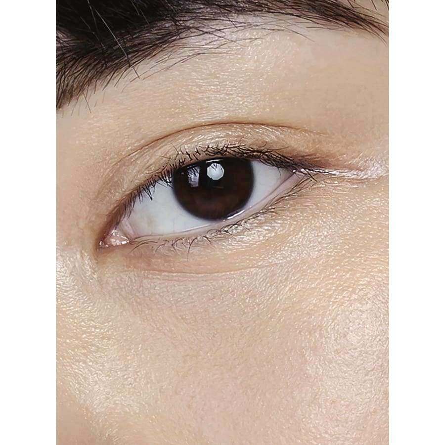 MÁDARA The Concealer, sävy Honey; lähikuva henkilön oikeasta silmästä, sileä, vaalea iho ja tumma, selkeärajainen kulmakarva; silmä avoinna ja katse eteenpäin; ei näkyvää tuotetta, pakkausta tai taustaa.