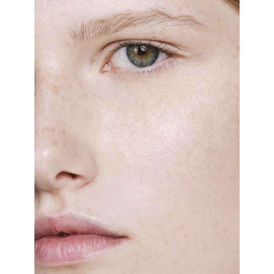 MÁDARA The Concealer, sävy Vanilla; lähikuva henkilön kasvoista, puhdas iho vaalein pisamin, vihreät silmät ja vaaleanpunaiset huulet; kuvan tarkennus silmässä, poskessa ja osassa nenää, korostaen vihreiden silmien sävyä; ei näkyvää tuotetta tai pakkausta; taustaa ei näytetä; ei etikettejä, tekstiä tai käsivuorovaikutusta.