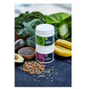Plantforce Magnesium Maustamaton; kaksi purkkia tekstillä "Magnesium" pinottuna sileälle alustalle, mattapintaisina yksinkertaisella groteskikirjasimella; ympärillä lehtivihanneksia, banaaneja, parsakaalia, avokadopuolikkaita, chiansiemeniä ja erilaisia pähkinöitä; kirkkaasti valaistu pöytäasetelma, ei ihmisiä tai käsiä kuvassa.