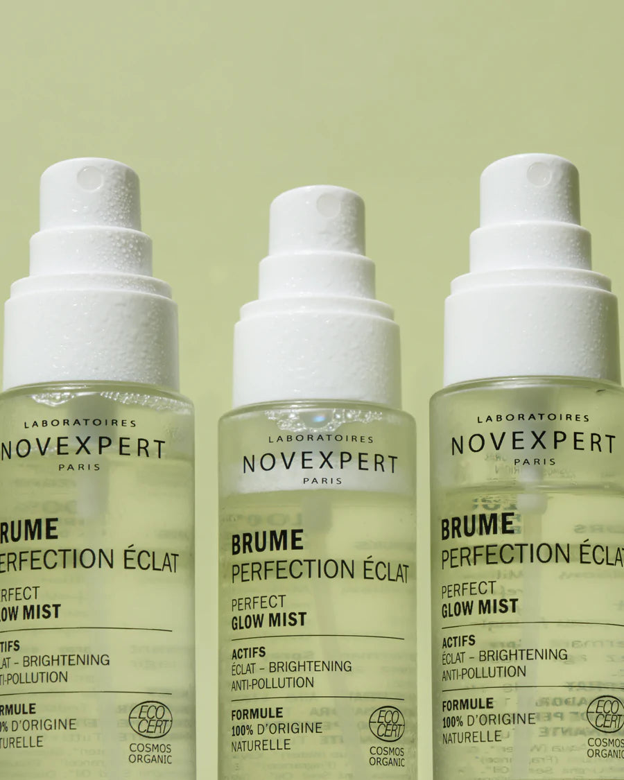 Novexpert POLYPHENOLS Perfect Glow Mist; kolme lieriön muotoista, läpinäkyvää pulloa valkoisin suihkepäin rivissä vaaleanvihreää taustaa vasten, sisällä väritöntä nestettä osittain täytettynä; valkoisilla suorakulmaisilla etiketeillä mustaa ja oranssia groteskitekstiä.