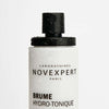 Novexpert HYALURONIC Smoothing Toning Mist; lähikuva valkoisesta muovisesta suihkupullosta tekstillä "Brume Hydro-Tonique", vesipisaroita näkyvissä mustalla mattapintaisella suuttimella ja pullon yläosassa; etiketin teksti mustalla groteskikirjasimella ja pientä oranssia yksityiskohtaa; pullo sylinterinmuotoinen; valkoinen tausta, ei ihmisiä tai käsiä.