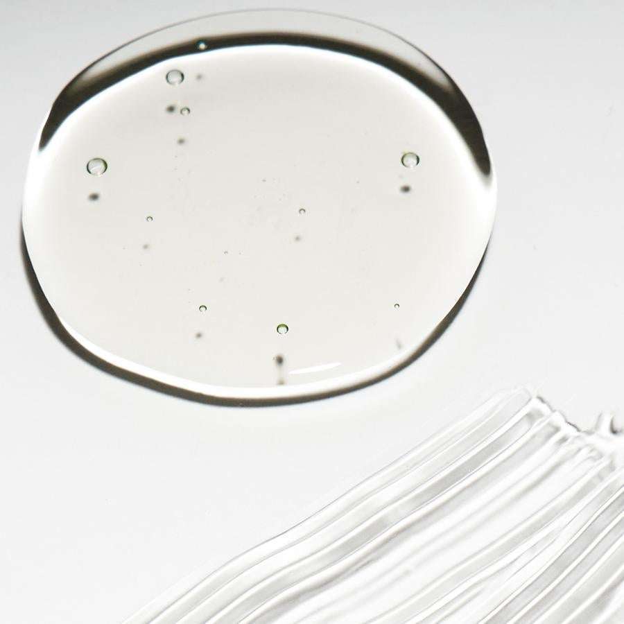 Novexpert HYALURONIC Booster Hyaluronihapposeerumi; kirkas geelimäinen neste pieniä ilmakuplia sisältävänä pyöreänä lammikkona sekä ohuina raitoina levitettynä sileälle valkoiselle alustalle; ei näkyvää pakkausta, brändäystä tai tekstiä; mattapintainen tausta; kuva tiiviisti rajattu tuotteen tekstuuriin, ei ihmisiä tai muita esineitä.