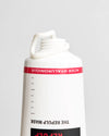 Novexpert HYALURONIC The Repulp Mask; lähikuva ylösalaisin käännetystä valkoisesta tuubista punaisella etiketillä tekstillä "ACIDE HYALURONIQUE"; yläosa auki paljastaen kierrekaulan ja irrotetun valkoisen korkin; pinta mattapintainen, teksti lihavoitua groteskikirjasinta; vaaleanharmaa tausta, ei ihmisiä tai toimintaa kuvassa.