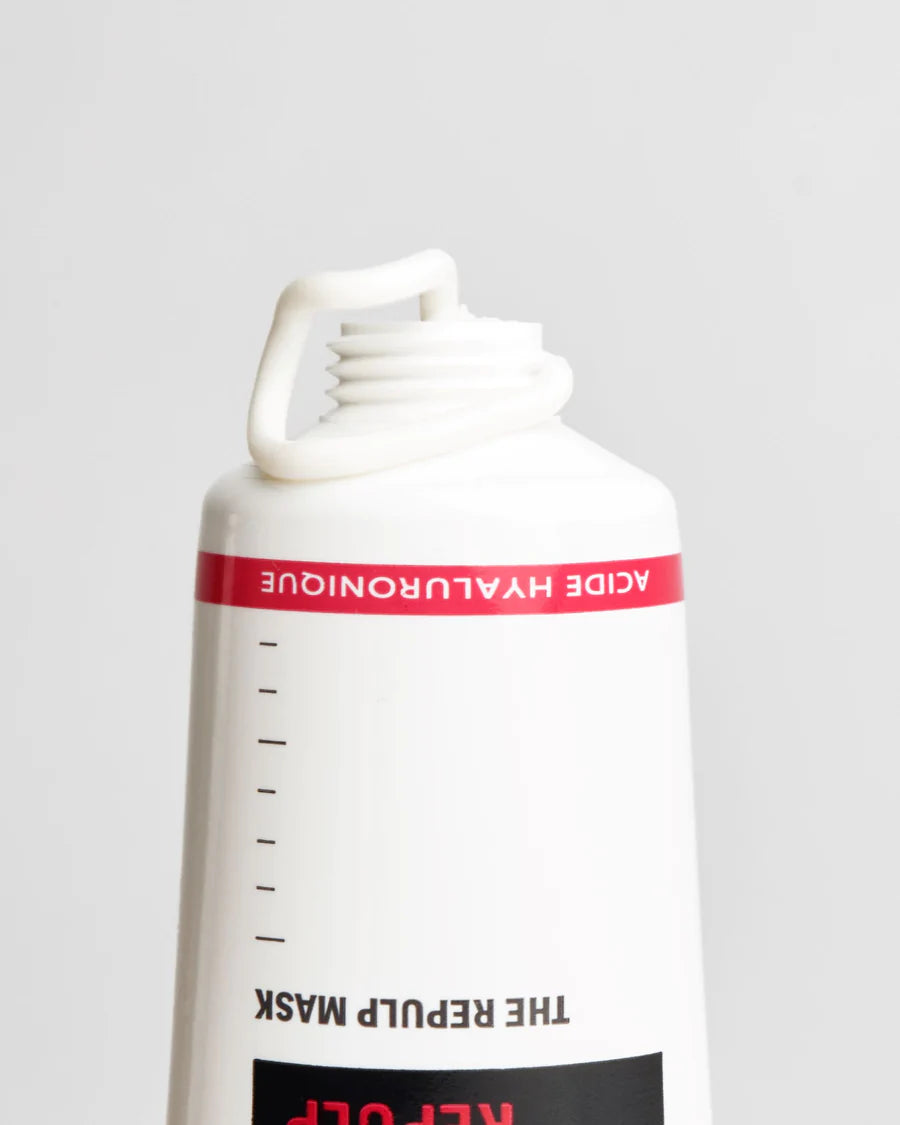 Novexpert HYALURONIC The Repulp Mask; lähikuva ylösalaisin käännetystä valkoisesta tuubista punaisella etiketillä tekstillä "ACIDE HYALURONIQUE"; yläosa auki paljastaen kierrekaulan ja irrotetun valkoisen korkin; pinta mattapintainen, teksti lihavoitua groteskikirjasinta; vaaleanharmaa tausta, ei ihmisiä tai toimintaa kuvassa.