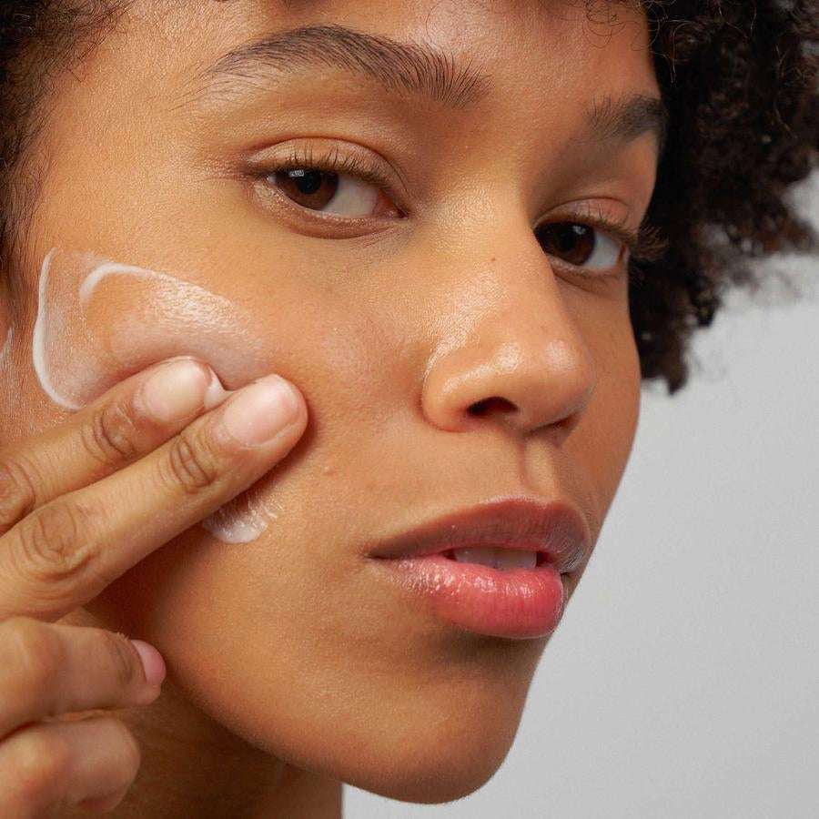 Novexpert TRIO-ZINC Purifying Gel; henkilö levittää varovasti pienen määrän hoitavaa voidetta poskelleen sormin katsoen suoraan kameraan; voide valkoista ja sileän tekstuurista; pakkaus ei näy kuvassa; tausta pehmeä ja neutraali ilman selkeitä esineitä; lähikuva muotokuvana.