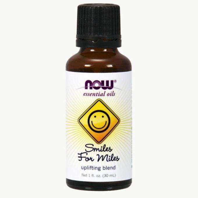 NOW Essential Oils Smiles for Miles -piristävä öljyseos, 1 fl. oz. (30 mL); ruskea, lieriömäinen, kiiltäväpintainen lasipullo, musta kierrekorkki; etiketissä keltainen hymyilevä kasvokuva sekä selkeää groteskitekstiä; ei ihmisiä; vaalea tausta, tuote keskitettynä kuvassa.