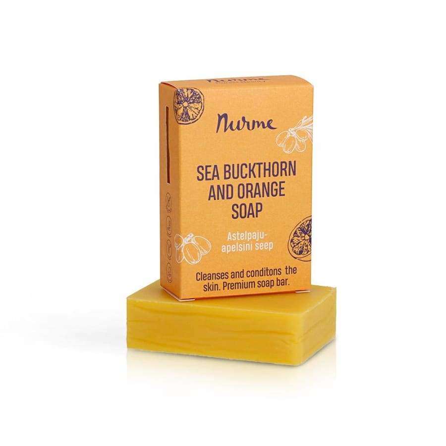 Nurme Tyrni & Appelsiini -palasaippua; suorakulmainen keltaoranssi saippuapala valkoisella pinnalla, päällä pystyssä oranssi rasia tekstillä "Nurme Sea Buckthorn and Orange Soap"; rasiassa marjakuvituksia sekä kaksikielistä tekstiä englanniksi ja viroksi tyrnistä; molemmat mattapintaisia; ei ihmisiä tai käsiä; tuotekuva vaalealla taustalla.