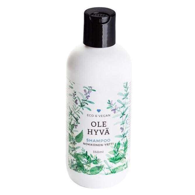 OLE HYVÄ Shampoo Nokkonen-Yrtti -pullo, 350 ml; valkoinen, mattapintainen ja sylinterimäinen pullo mustalla korkilla suorin sivuin ja pyöristetyin olkapäin; valkoisessa etiketissä vihreitä kasvikuvituksia ja mustaa modernia tekstausvapaata tekstiä; kuvattu silmän korkeudelta neutraalia taustaa vasten, ei ihmisiä tai käsiä näkyvissä.