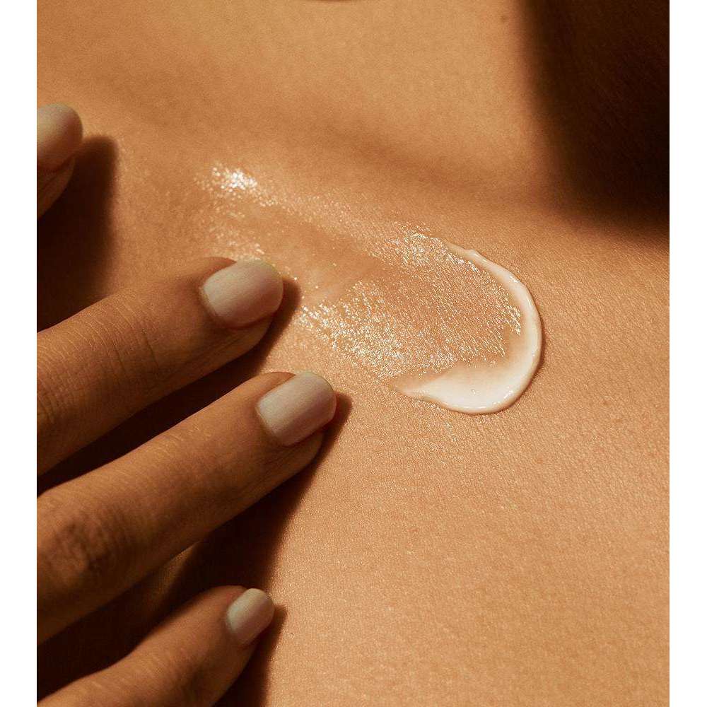 Patyka Face Sun Cream SPF50+ Aurinkovoide kasvoille; siististi manikyroidut kynnet omaava käsi levittää lempeästi voidenokareen sileälle, ruskettuneelle iholle, viitaten ravitsevaan ihonhoitorutiiniin; voide valkoista ja paksuhkoa; ei näkyvää pakkausta tai brändausta kuvassa; tausta neutraali ja epätarkka; lähikuva keskittyy voiteen levittämiseen iholle.