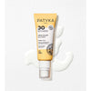 Patyka Face Sun Cream SPF30 Aurinkovoide kasvoille; tuubi PATYKA Paris SPF 30 -aurinkovoidetta keltaisella korkilla lepää valkoisella pinnalla valkoisten voidepyörteiden ympäröimänä; matta tuubi näyttää mehiläiskennokuviointia etuosassa ja sekä groteski- että serif-tekstiä, mukaan lukien tuotenimi, "SPF 30", "antioxidant formula" ja "broad-spectrum"; ei ihmisiä tai käsiä näkyvissä.