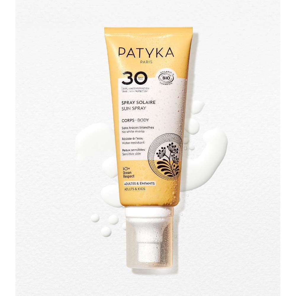 Patyka Sun Body Milk SPF30; tuubi Patyka Paris 30 SPF -aurinkovartalosuihketta esillä pystyssä, kaksisävyinen keltainen ja valkoinen matta suunnittelu yksinkertaisin mustin groteskitekstein; tuote valkoisella taustalla, vieressä näkyvä aurinkovoiteen läikkä ja useita hajanaisia nestepisaroita; etikettiteksti sisältää tuotenimen, SPF-tason ja maininnan sopivuudesta aikuisille ja lapsille; ei ihmisiä tai käsiä näkyvissä.