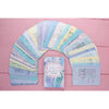 A set of colorful, pastel affirmation cards is arranged in a semicircle on a pink wooden surface, with one uplifting card deck box in the center. The cards have smooth matte finishes and rounded corners, displaying assorted soft colors including blue, green, yellow, and pink. The box matches the color scheme and sits upright. Typography varies by card but includes modern sans-serif fonts in white or dark hues. No people or hands are visible in the shot. Cards include legible phrases such as “You are