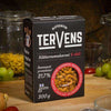 Tervens Kikhernemakaroni & Chili -pakkaus puisella pöydällä; ympärillä pastalla täytettyjä lasipurkkeja, vihreitä viinirypäleitä ja punaisia tomaatteja; pakkauksessa tekstausvapaata tekstiä, mattapintainen viimeistely sekä luettavissa teksti "gluten-free" ja "high protein"; ei ihmisiä kuvassa.