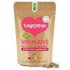 Together Health Woman's Multi; ruskea mattapintainen uudelleensuljettava pussi tekstillä "Together Woman's Multi Vit & Mineral Whole Food Supplement"; etiketissä selkeitä kuvia vihanneksista sekä tiivis teksti 30 kasviskapselista, raa'oista ainesosista ja mahalle lempeydestä; kaksi ruskehtavaa kapselia pussin edessä; vaalea tausta, ei ihmisiä tai käsiä kuvassa.