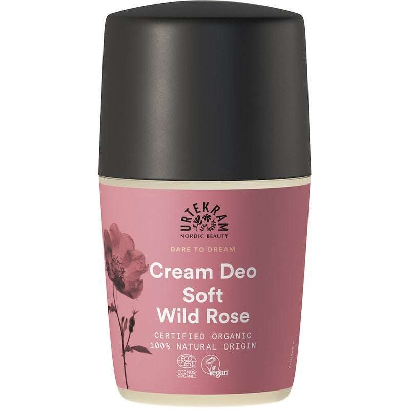 Urtekram Dare to Dream Soft Wild Rose Deodorantti; pullo mustalla korkilla ja vaaleanpunaisella etiketillä, merkitty luomusertifioiduksi, vegaaniseksi ja 100-prosenttisesti luonnollista alkuperää olevaksi; etiketissä hienovarainen ruusukuvitus; pullo sylinterinmuotoista muovia mattapintaisena, selkeä groteskikirjasin; korkki sileää ja opaakkia mustaa muovia; valkoinen tausta pehmein varjoin, suoraan edestä otettu tuotekuva, ei ihmisiä.