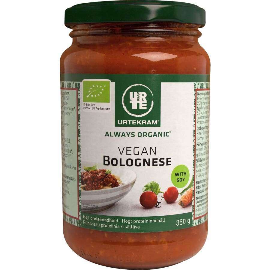 Urtekram Vegan Bolognese -kastikepurkki, 350 g, soijapohjainen; sylinterimäinen kirkas lasipurkki metallisella kiertokannella; mattapintaisessa etiketissä vihreää ja punaista, valkoista ja mustaa tekstausvapaata tekstiä, merkintä "Always Organic"; etiketissä kuva pastasta tomaattikastikkeen kanssa sekä luomusertifiointimerkkejä; kuvattu valkoista studiotaustaa vasten, ei ihmisiä tai käsiä näkyvissä.