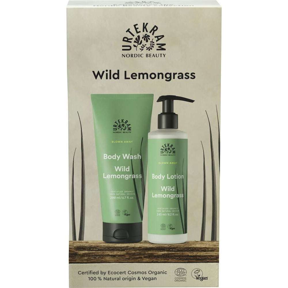 Urtekram Blown Away Wild Lemongrass Lahjapakkaus; suihkuvoide- ja vartalovoidetuubit mattapintaisen vihreinä, molemmat pystyssä suorakulmaisessa beigessä pahvipakkauksessa; laatikossa teksti "Nordic Beauty" lihavoidulla groteskikirjasimella; tuubeissa luettavissa brändinimi, tuoksu ja luomusertifiointimerkinnät; ei ihmisiä tai toimintaa, tasainen studiotausta, suoraan edestä otettu kuva.