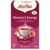YogiTea Luomu Womens Energy -teepakkaus; suorakulmainen, mattapintainen ja vaaleanpunainen rasia; etiketissä kuvat teekupista, inkivääristä ja hibiskuksesta; valkoisella ja tummanpunaisella tekstillä yksinkertaisella tekstaus- ja päätekirjasimella maininnat luomusta, kofeiinittomuudesta ja 17 teepussista; kuvattu suoraan edestä yksiväristä taustaa vasten, ei käsiä tai ihmisiä näkyvissä.